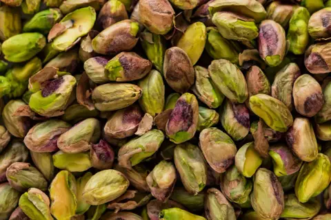 Zbliżenie na stos łuskanych pistacji, niektóre z zielonymi nasionami, inne z brązowymi łupinami.